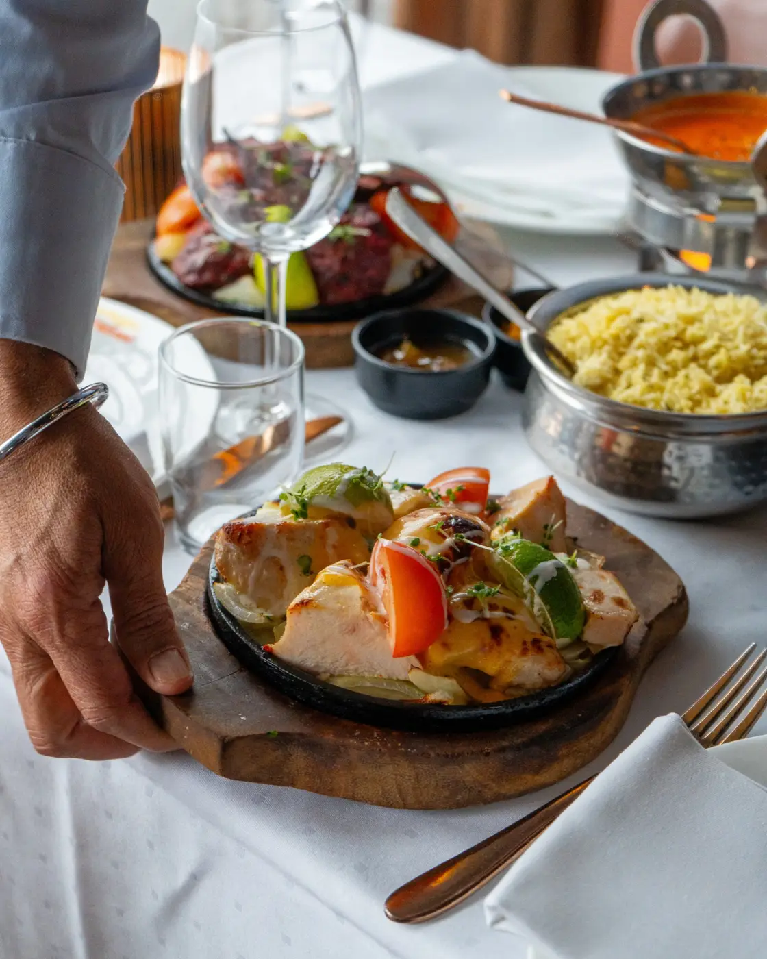 Tandoorirett servert sizzlende på trefat med ris og saus
